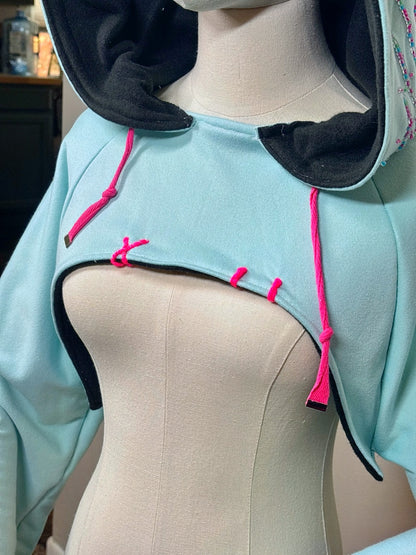 Light blue hoodie with black cuffs and pink drawstrings on a mannequin against a beige background. Inspired by  Vanellope von Schweetz from Disney's Wreck it Ralph. Perfect Cosplay Shrug.